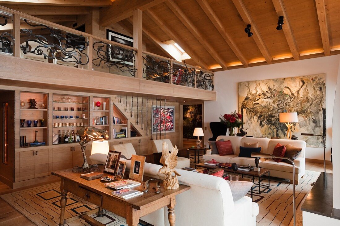 Grossräumiges Wohnzimmer mit Sofagarnitur gegenüber Einbauschrank unter Galerie mit Blick in den Dachstuhl