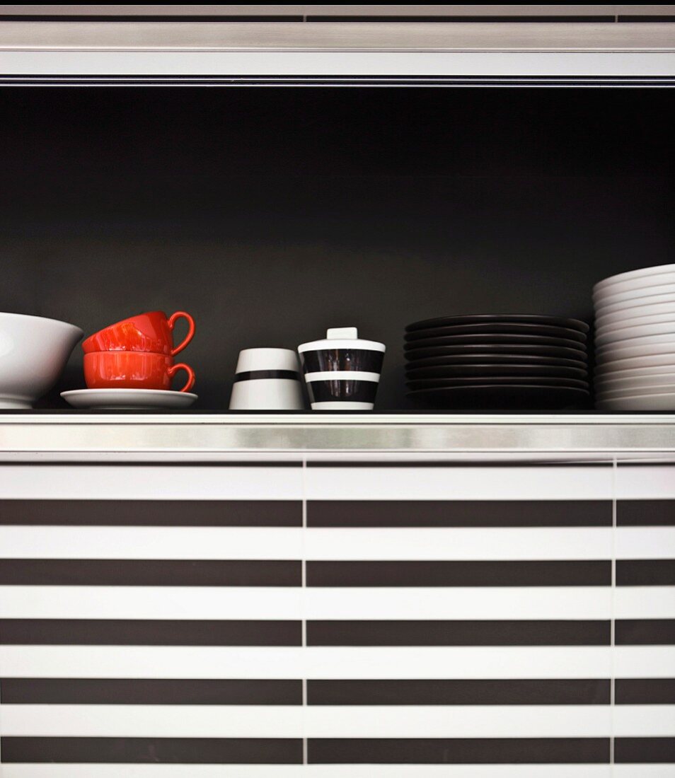 Ausschnitt eines Hängeschranks mit Geschirr vor schwarzer Rückwand, Küchenwand mit schwarz-weißen horizontalen Streifen