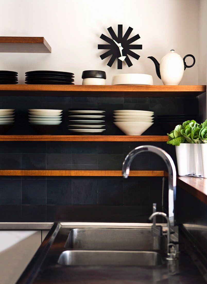 Kitchen shelves on dark grey tiled wall next to stainless steel sink