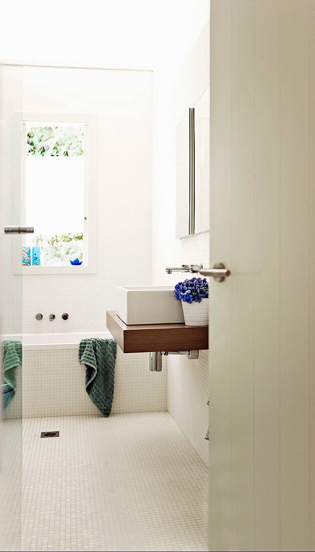 Blick in ein weisses Badezimmer mit Waschtisch und Badewanne unter dem Fenster