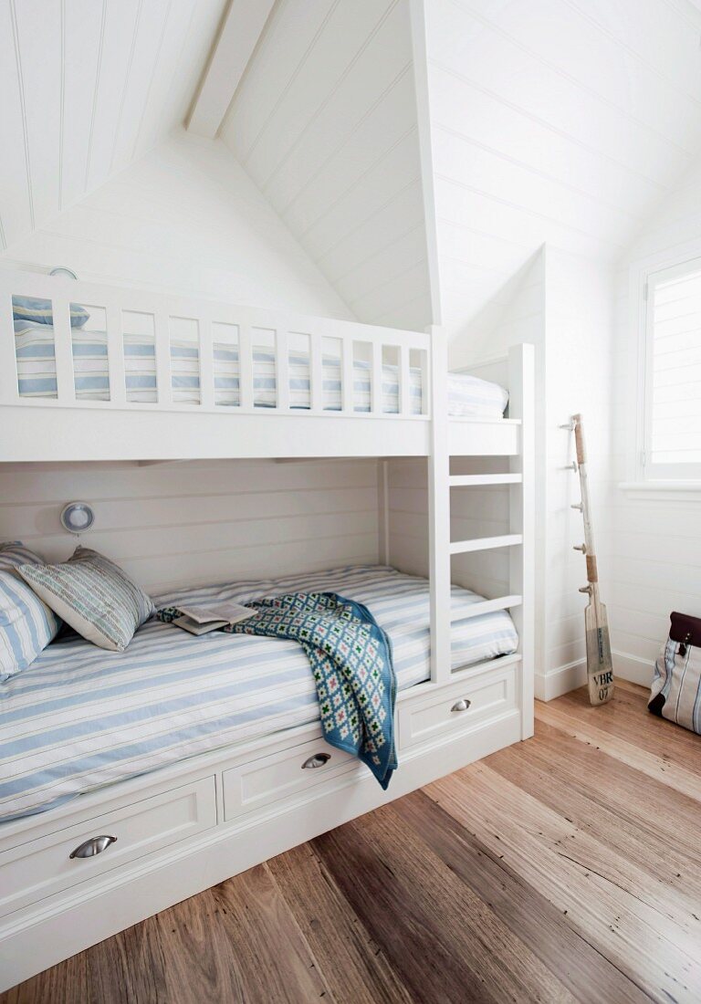 Bedroom with white bunk beds and blue and white striped bed linen in attic room with dark wooden floor