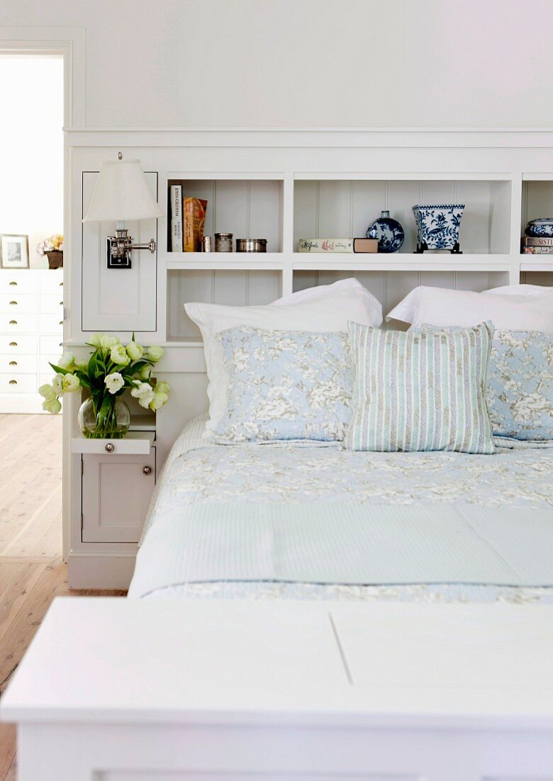 White, fitted shelving integrated in headboard of double bed