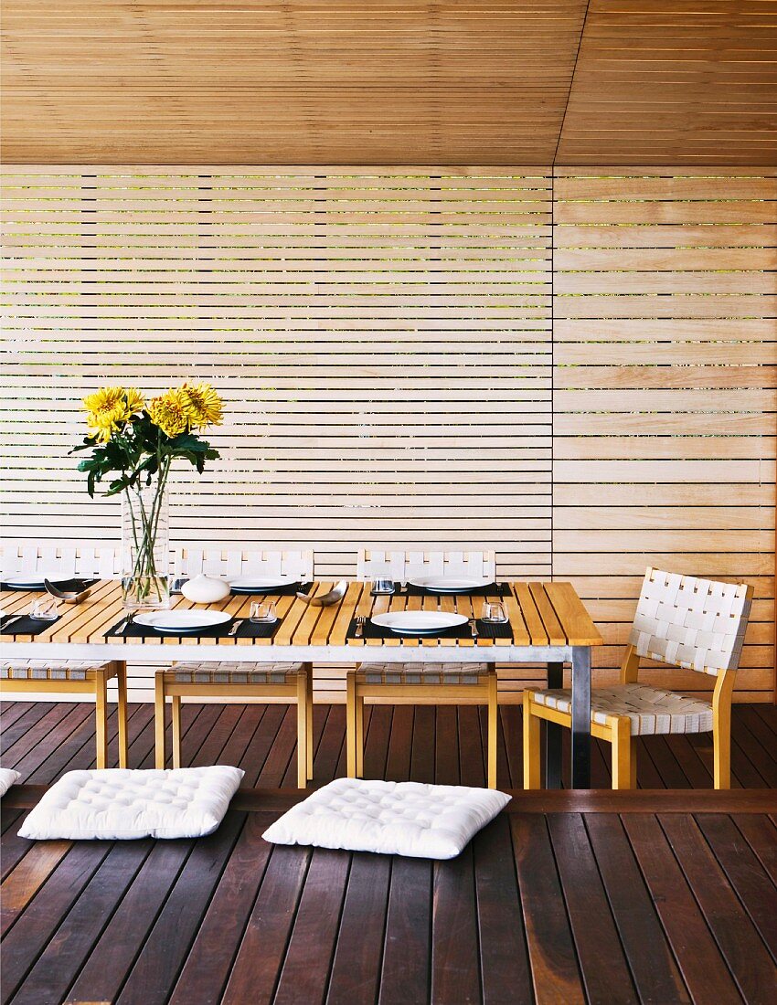 Überdachte Terrasse eines Holzhauses mit gedecktem Tisch und Holzbank