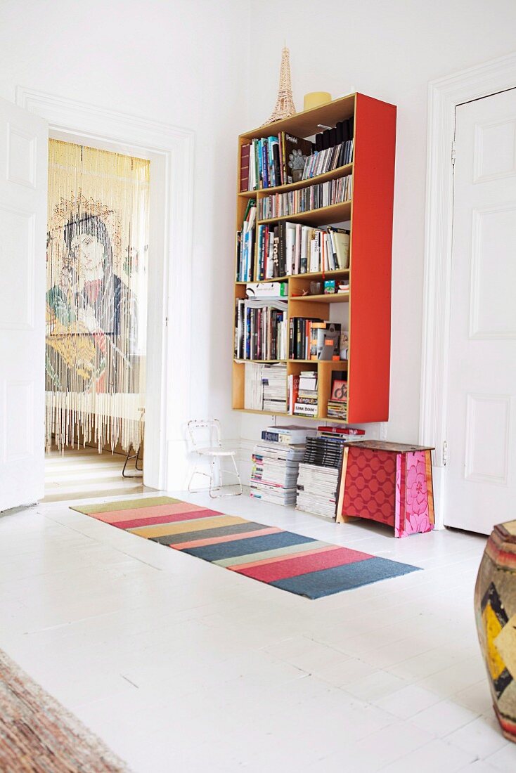 Red bookcase in white-painted room next to thread curtain in doorway