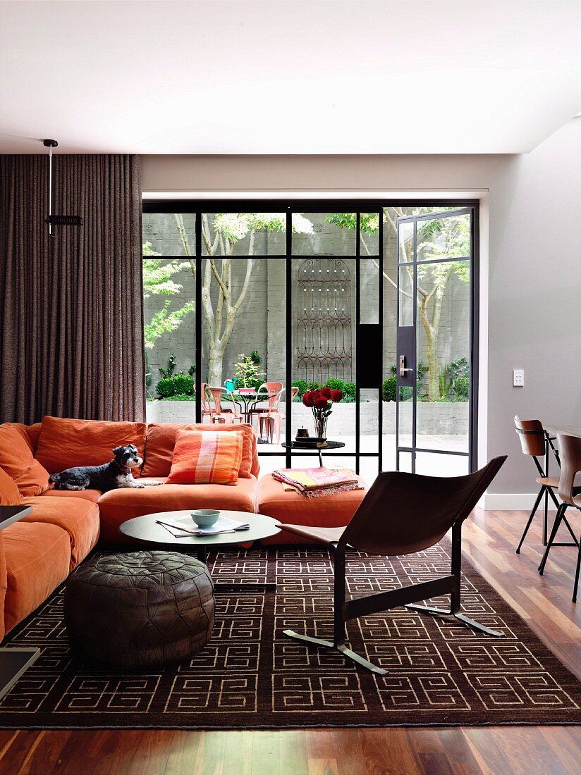 Stuhl im 50er Jahre Stil und gemütliches oranges Sofa vor Glasfront mit Blick auf Terrasse