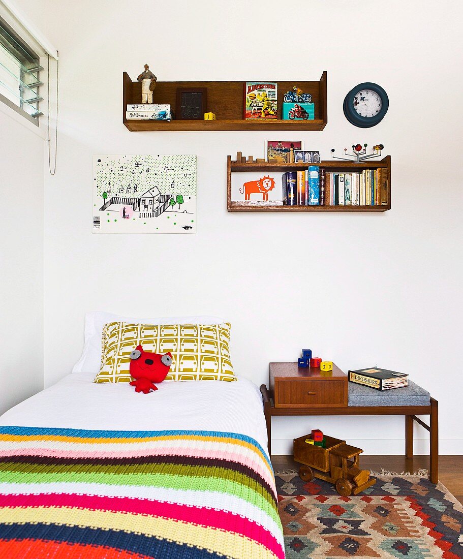 Bett mit gestreifter Tagesdecke unter Wandregal im Kinderzimmer
