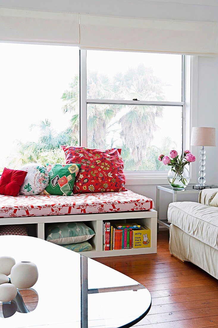 Bench with storage space, colourful scatter cushions and seat cushion below window in bright living area