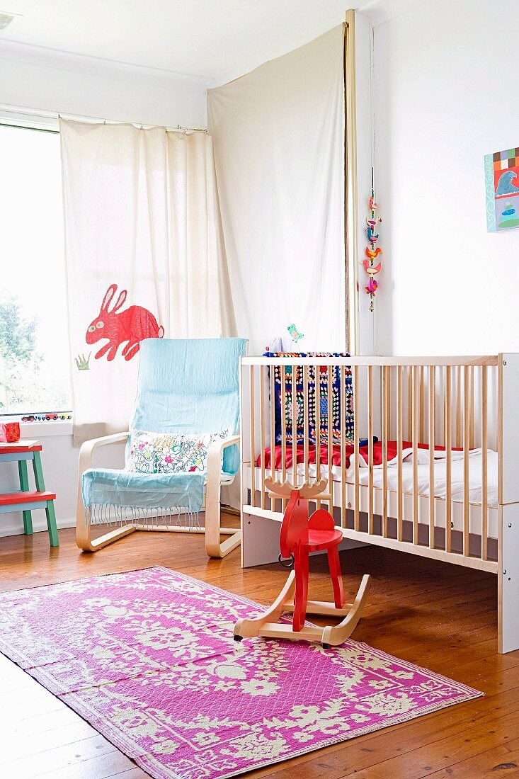 Helles Kinderzimmer mit Gitterbett, hellblauem Freischwingersessel und rotem Schaukeltier