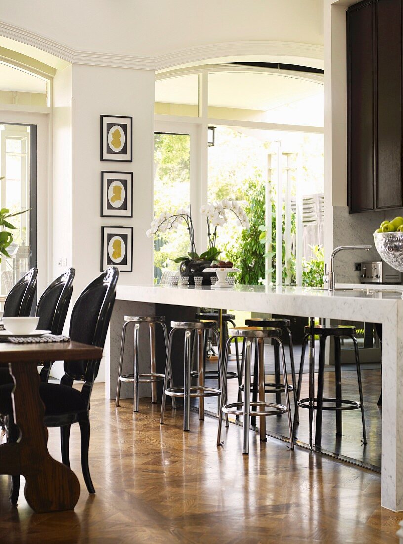 Hocker vor Küchenbar und rustikaler Esstisch mit schwarzen gepolsterten Stühlen
