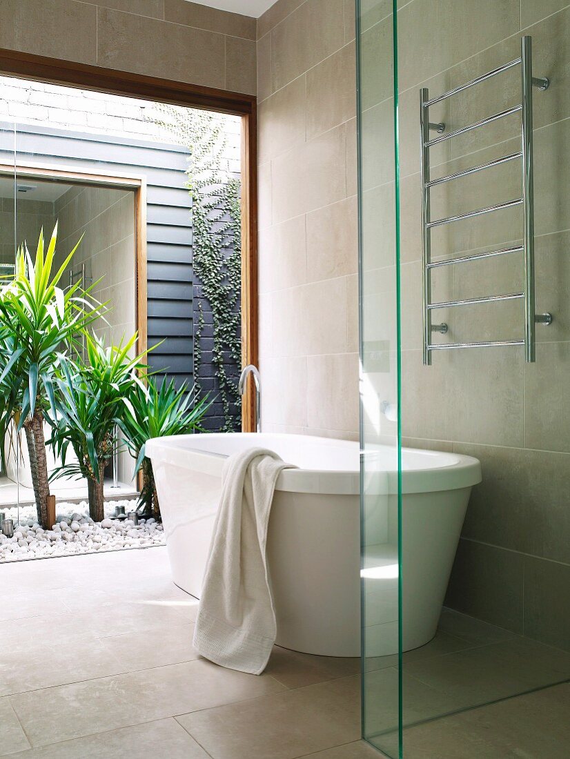 Freistehende Badewanne vor Panoramafenster zum gekiesten Innenhof mit Yuccapalmen