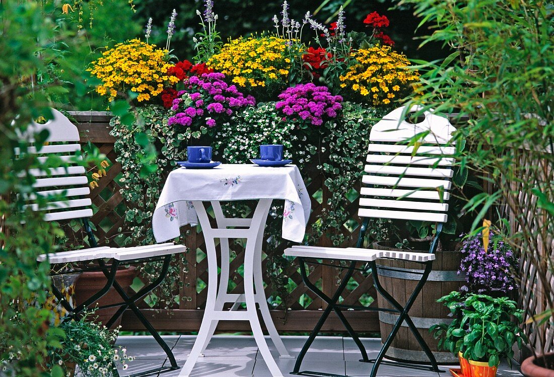 weiße Stühle und Tisch vor Blumenkasten auf einem Balkon