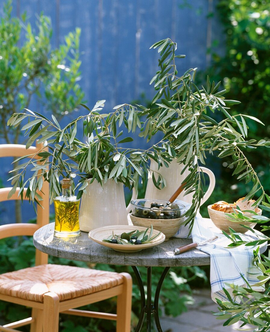 Schwarze und grüne Oliven, Olivenöl mit Rosmarin und Olivenzweige auf einem Tisch im Freien