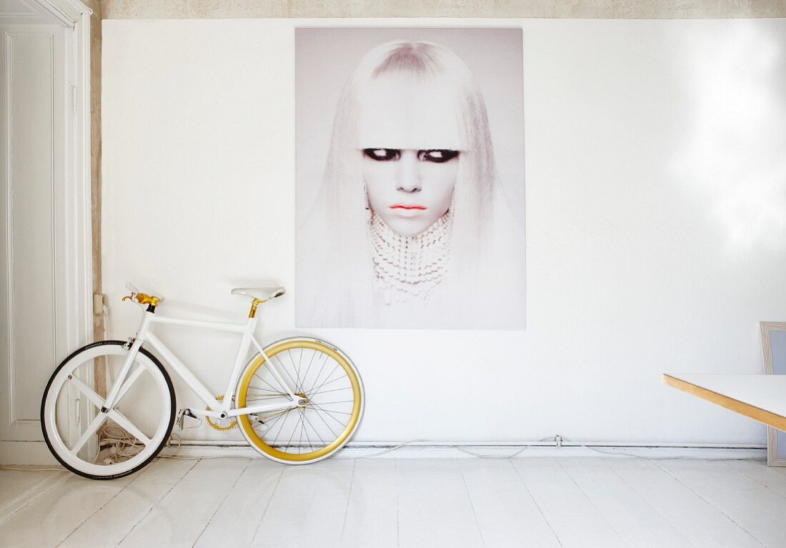 Bicycle below modern portrait of woman on wall in white artist's apartment