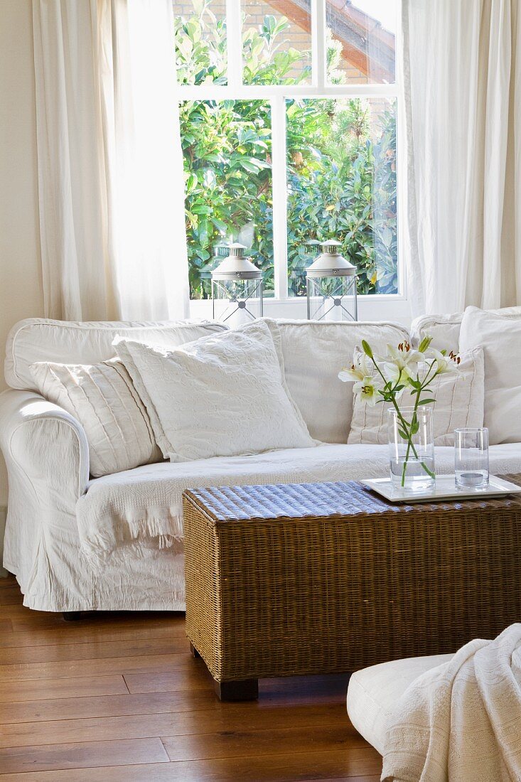 Weisses Sofa und Korbtisch vor dem Fenster