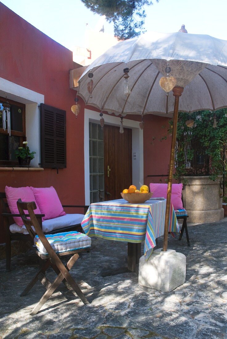Schattige Gartenterrasse im Nachmittagslicht mit dekorativem Sonnenschirm und gemütlicher Sitzgruppe darunter