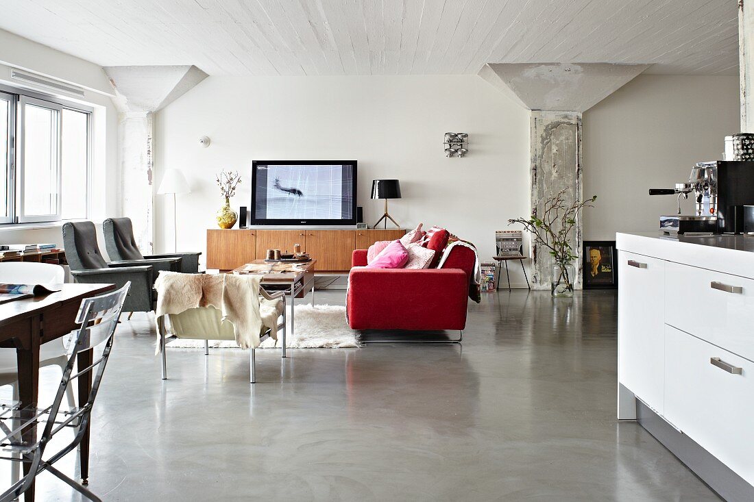 Loftartiger Wohnraum mit rotem Sofa im Loungebereich und offener Küche mit Essplatz