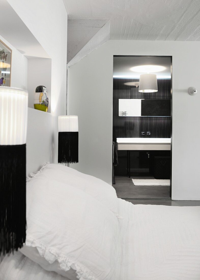 Black and white wall-mounted lamps either side of double bed with white bed linen and view into ensuite bathroom