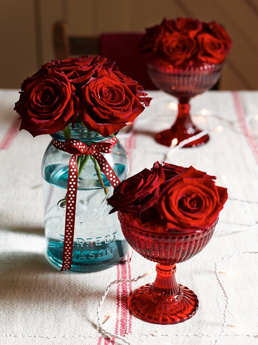 Red roses in glasses and jar