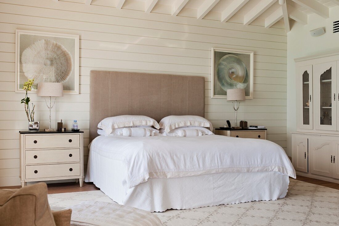 Imposantes, gepolstertes Kopfende eines Doppelbetts mit Schubladenkommoden als Nachttische in weißem Schlafzimmer