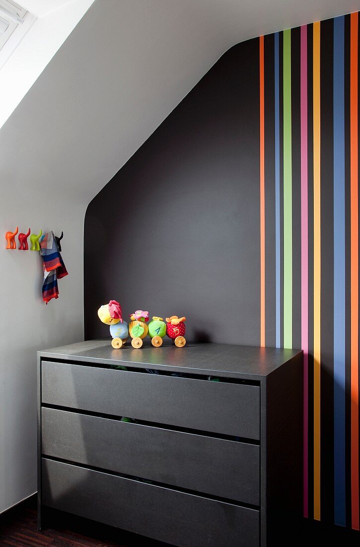 Black chest of drawers against black wall with multicoloured stripes in attic room