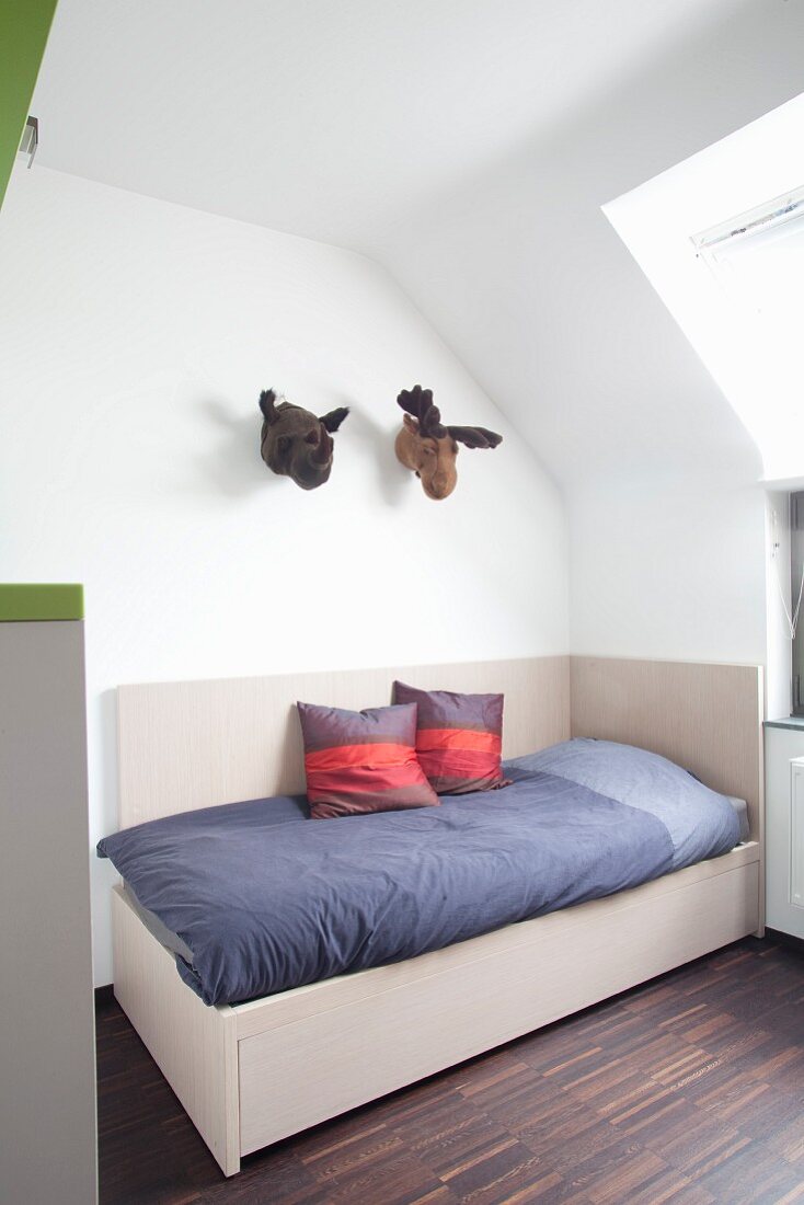 Bett mit hochgezogenem Holzrahmen im Kinderzimmer unter dem Dach