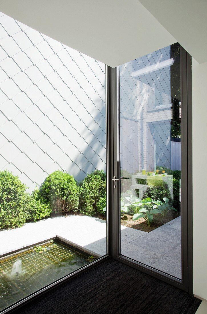 Blick durch Fensterfront in Innenhof mit Pflanzenstreifen vor Hauswand