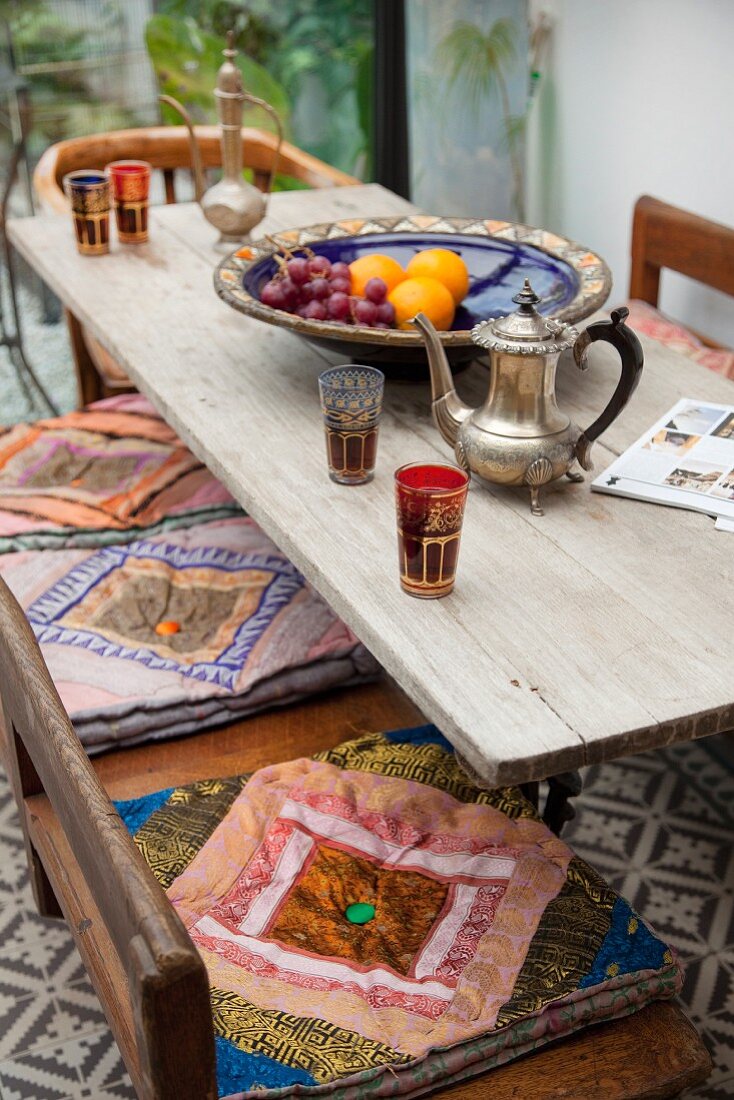 Holztisch mit orientalischer Teekanne und Gläsern und Holzbank mit bunten Sitzkissen