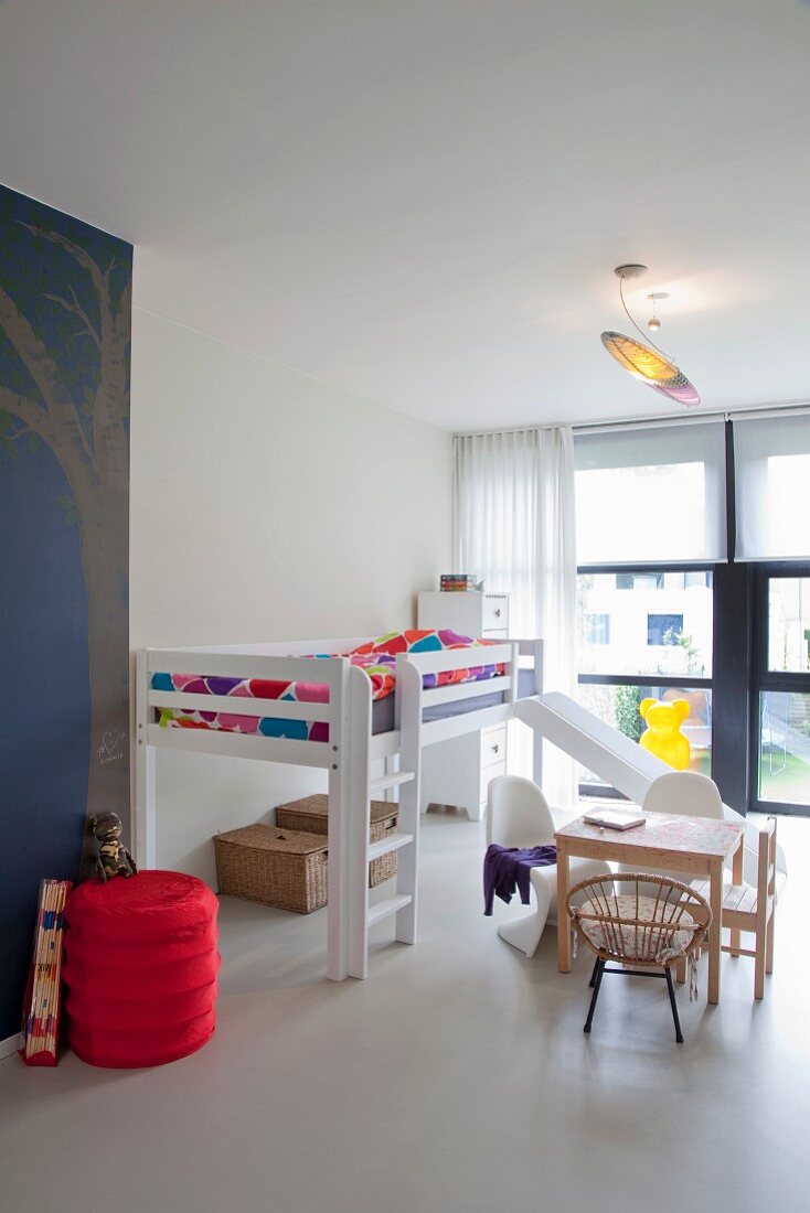 Loft bed with slide, child-size Panton chairs at small table and vintage trunks below bed in spacious child's bedroom