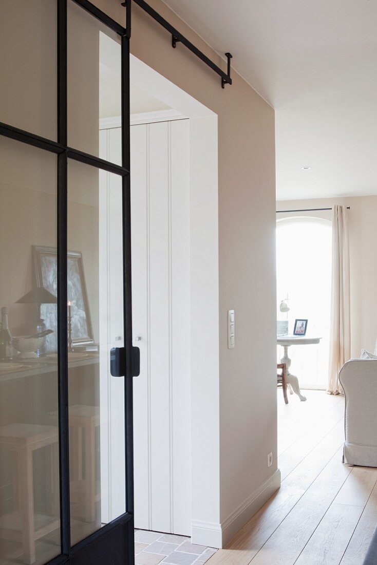 Glass sliding door with black metal frame in white interior with pale wooden floor