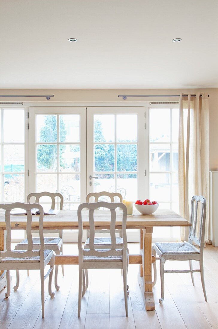 Ruhiges Esszimmer in klaren Naturfarben mit raumhoher Fensterfront, einem soliden Holztisch aus hellem Holz und weissen Vintage-Stühlen