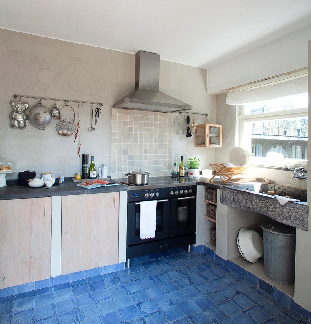Gemauerte Unterschränke und modernes Herdelement in einfacher Küche mit changierend blauen Bodenfliesen