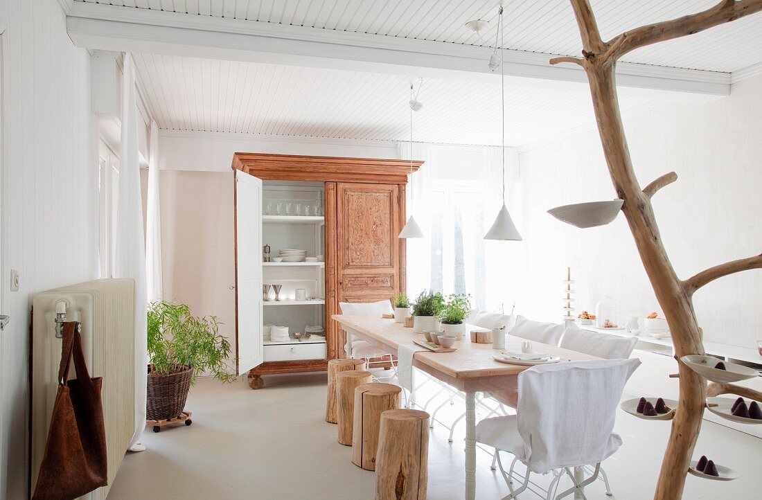 Gedeckter Tisch mit Baumstammhockern und Gartenstühlen mit Hussen; Kunstobjekt aus Baumstamm mit Porzellanschalen