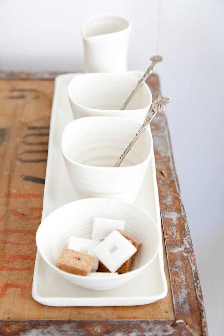 White tea bowls, silver spoons, sugar bowl and milk jug on long, narrow plate