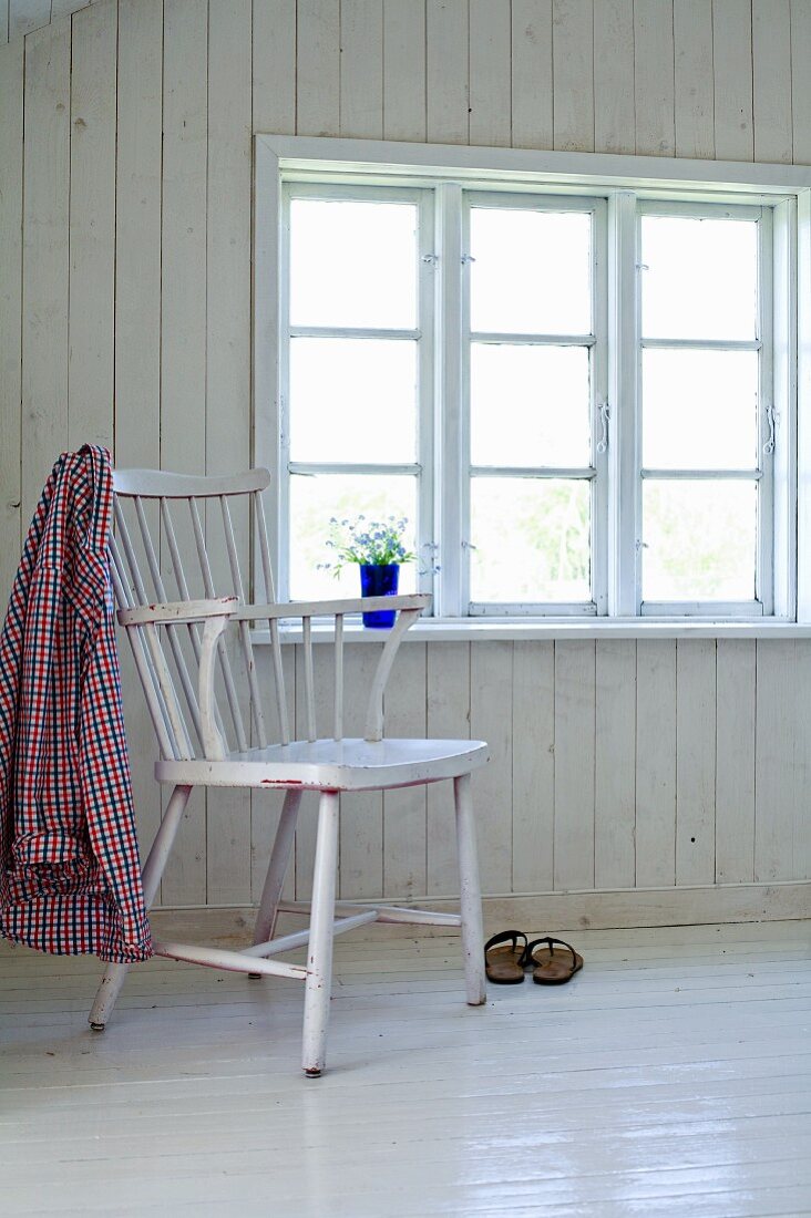 Hemd auf Lehne eines Stuhls gehängt in schlichtem Zimmer mit weiss gestrichenen Holzdielen
