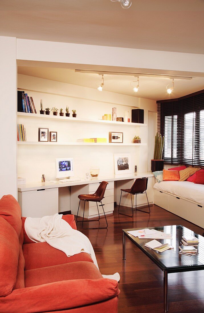 Einbaumöbel mit zwei Schreibplätzen und Bett in schräger Wohnraumnische; gemütliches Sofa im Vordergrund
