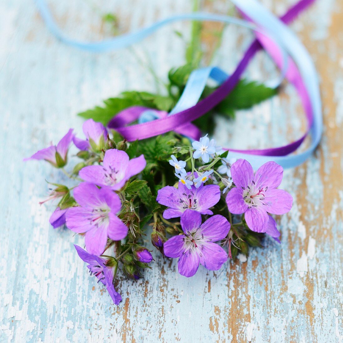 Purple flowers (cranesbill and forget-me-not) tied with ribbons on vintage wooden board