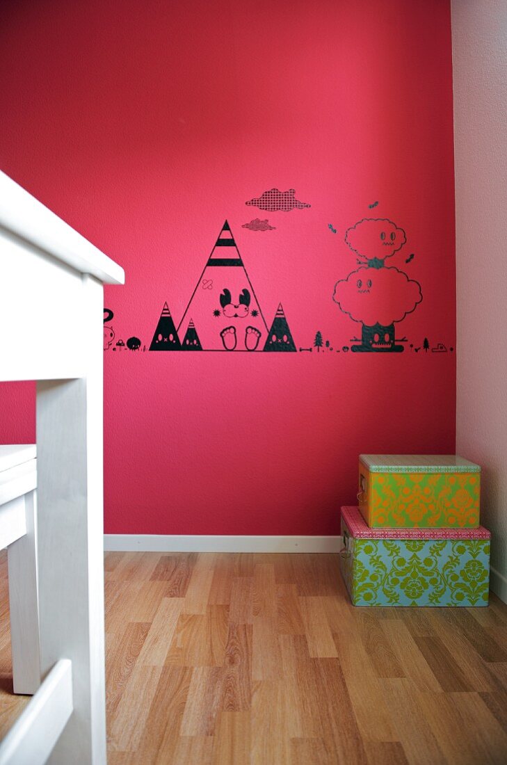 Pinkfarbene Wand mit schwarzen Zeichnungen und davorstehenden, gestapelten Aufbewahrungskisten