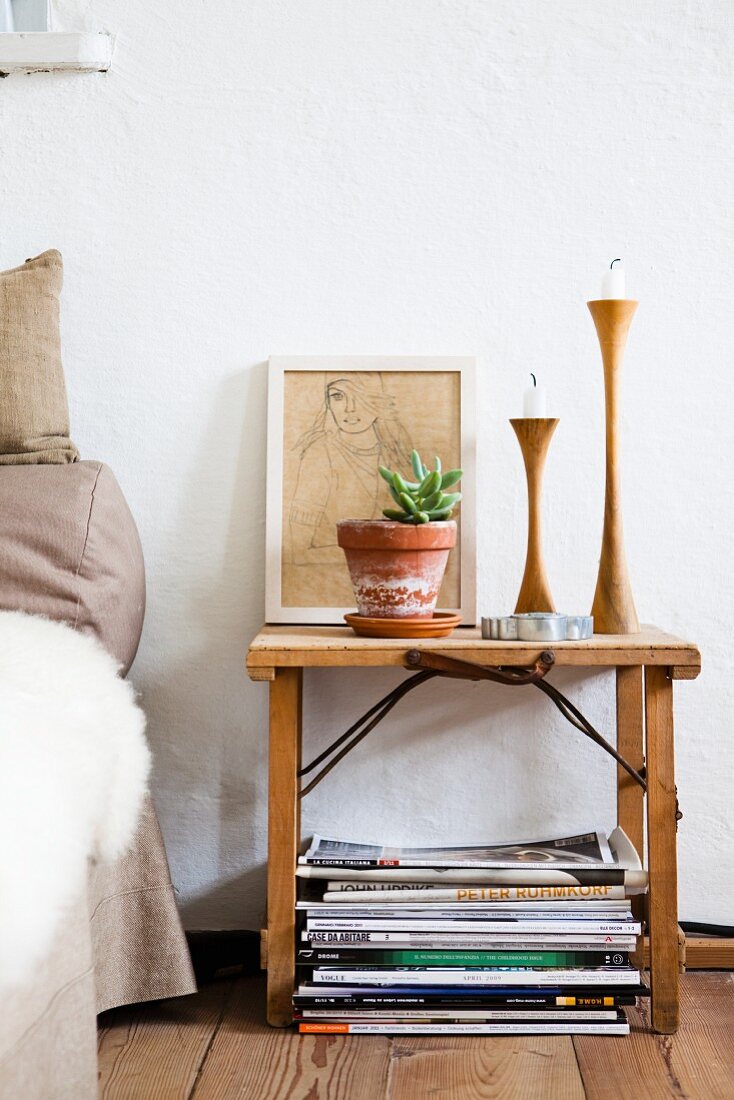 Houseplant, candlesticks and drawing on wooden bedside table in bedroom with wooden floor