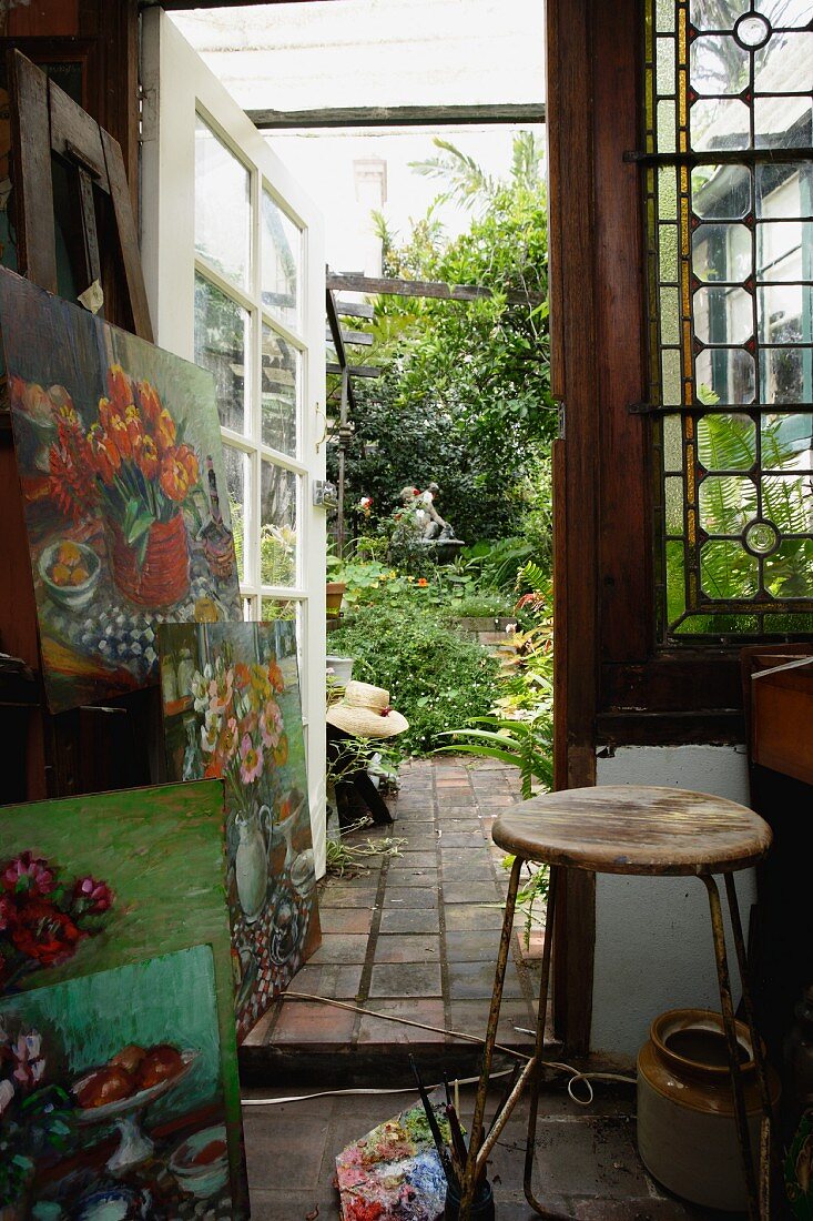Bilderstapel und Vintage Hocker im Atelier mit offener Glastür und Blick in den Garten