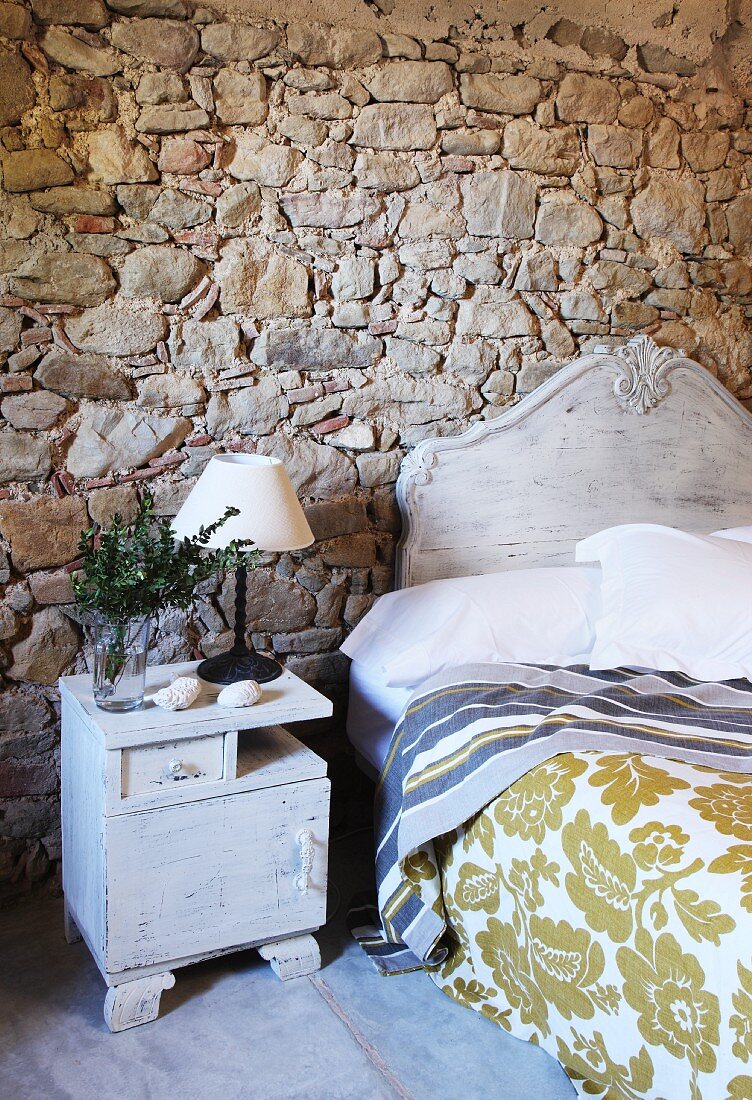 Weiß lackiertes Vintage Bett und Nachtkasten vor rustikaler Natursteinwand