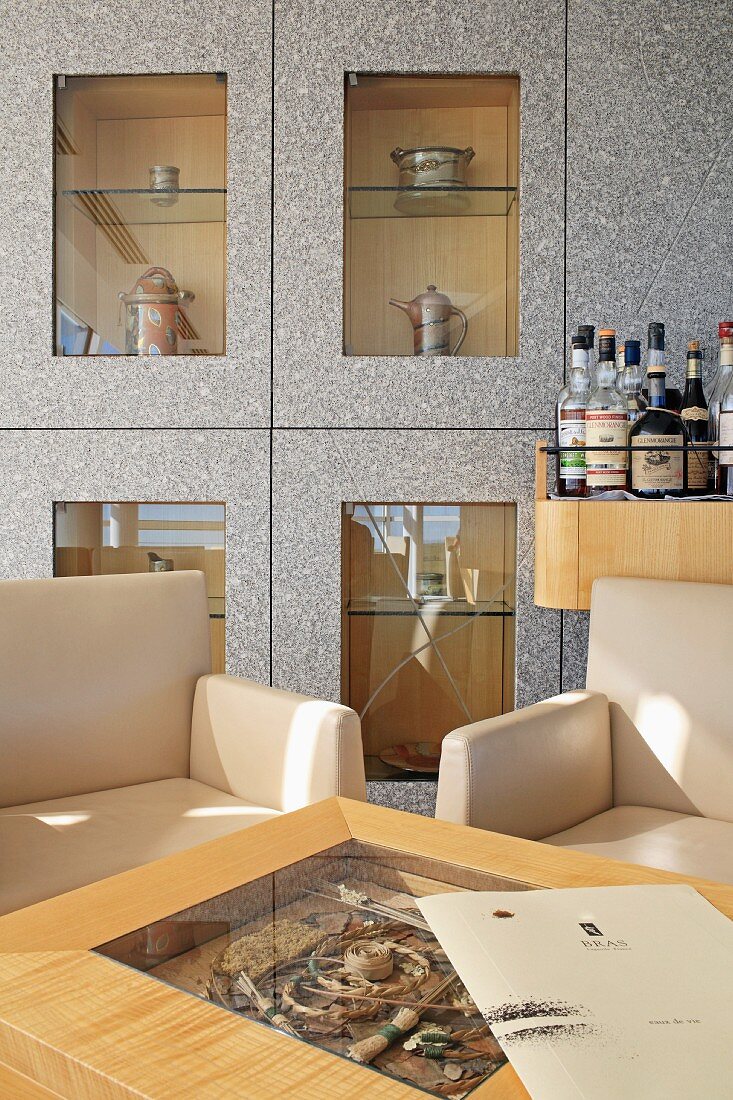 Elegant armchairs and table in front of bar and display case with separate, glass-fronted compartments