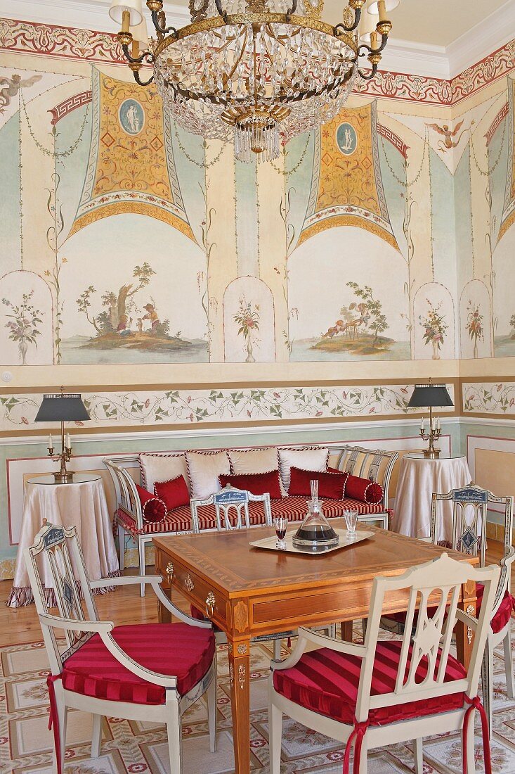 Antiker Tisch und hellgrau lackierte Stühle mit roten Polstern in herrschaftlichem Salon mit Wandbemalung
