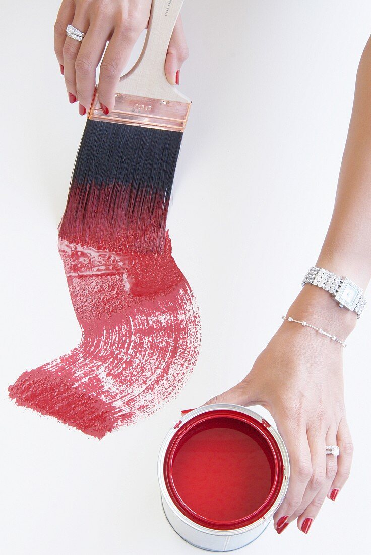 Hands of well-groomed woman wearing jewellery working with red paint and paintbrush