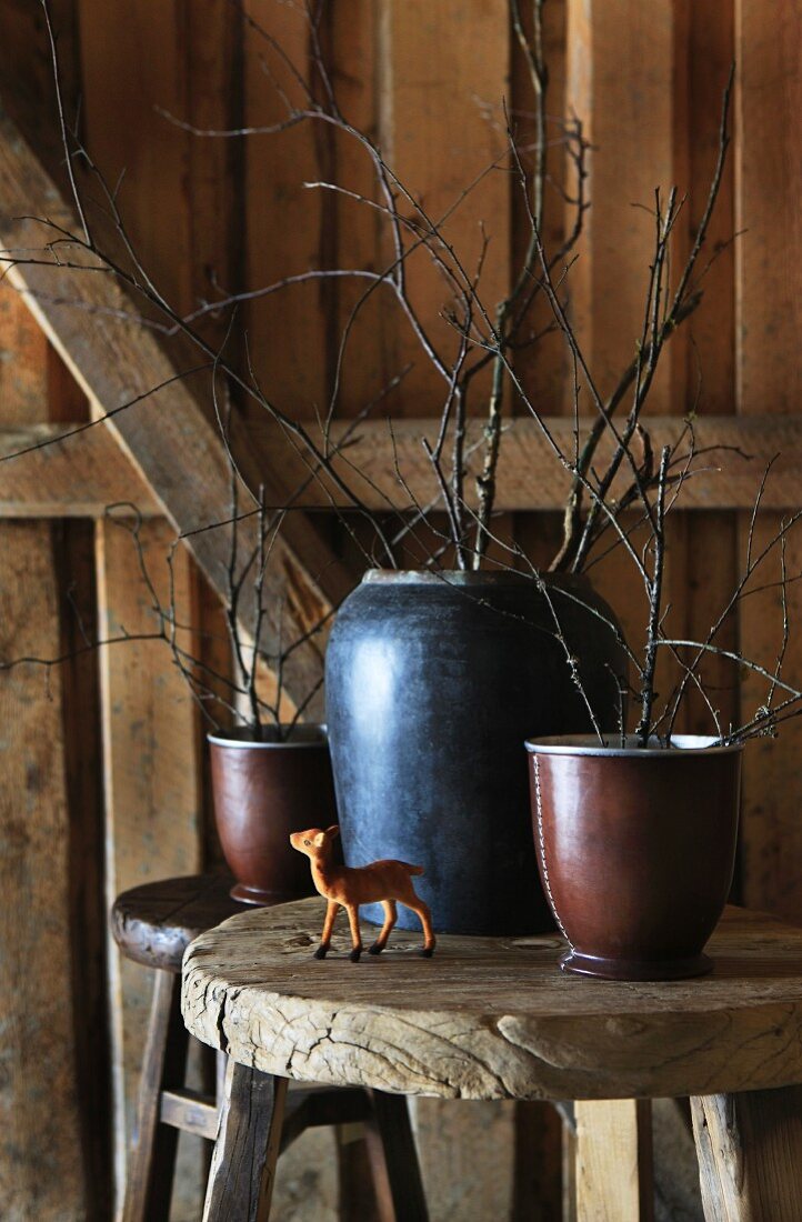 Kleine Rehfigur und Vasen mit Zweigen auf einem Holzhocker in einer Hütte