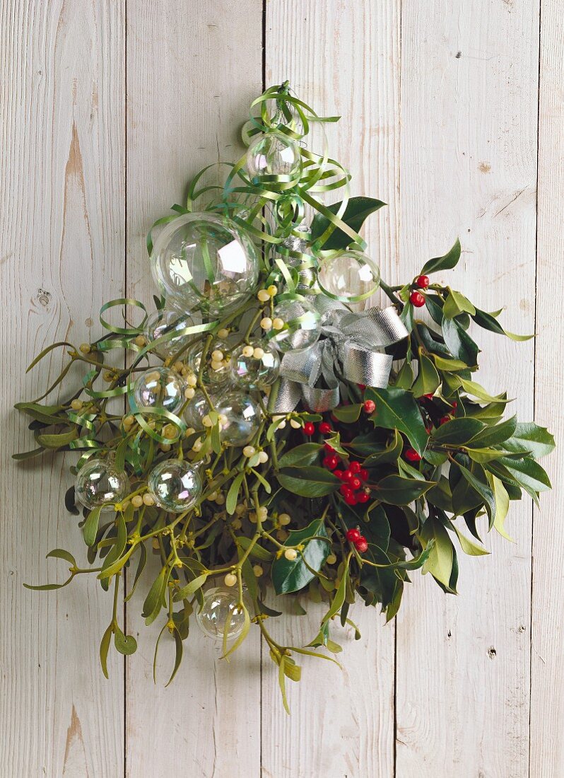 Weihnachtliches Arrangement aus Misteln und Ilexzweigen mit silberner Schleife und transparenten Glaskugeln