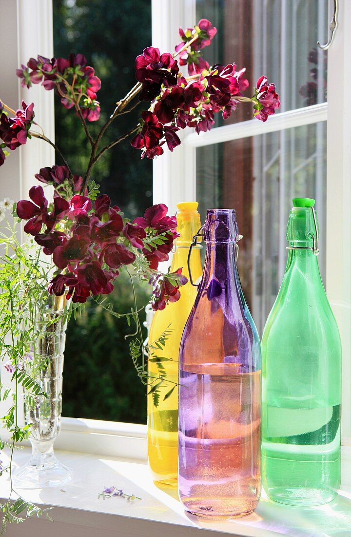 Colourful swing-top bottles and vase of flowers on window sill