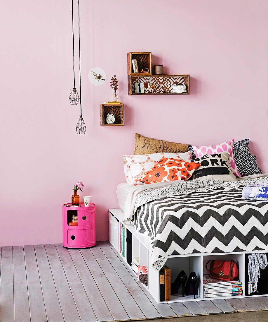 Bett mit vielen Stauraumlösungen, kleine Dekoregale an der Wand und Industrieleuchten über Nachttischbox in fröhlichem Pink
