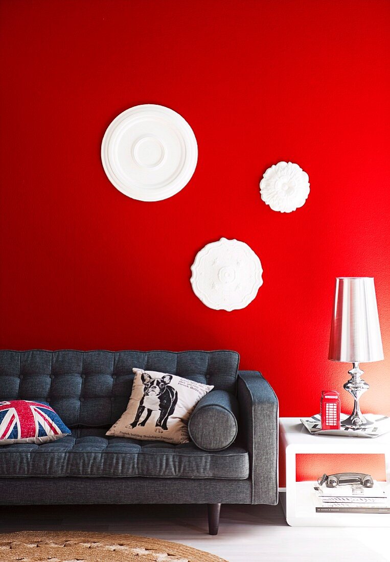 Stuckrosetten auf roter Wand über einem grauen Sofa