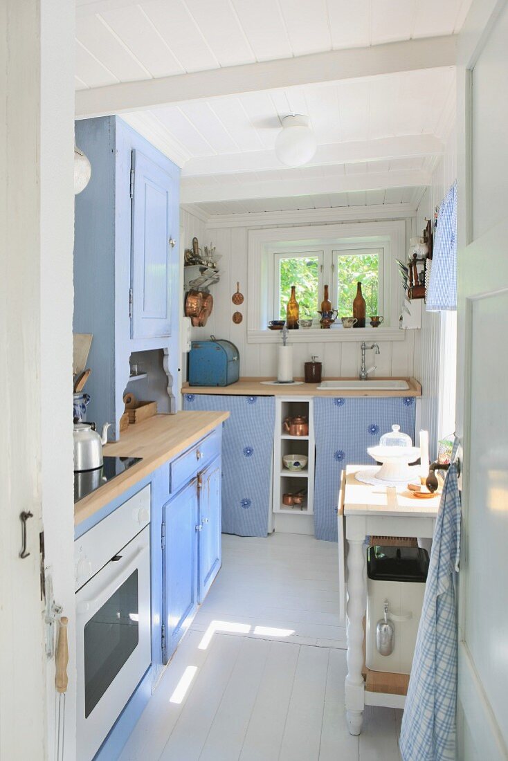 Freundliche Küche in Pastellblau mit weißen Bodenfliesen und hellen Holzflächen