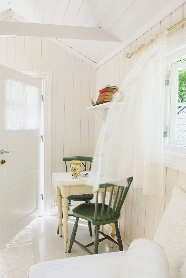 Chiffon curtains blowing in breeze in bright, summery room with open door